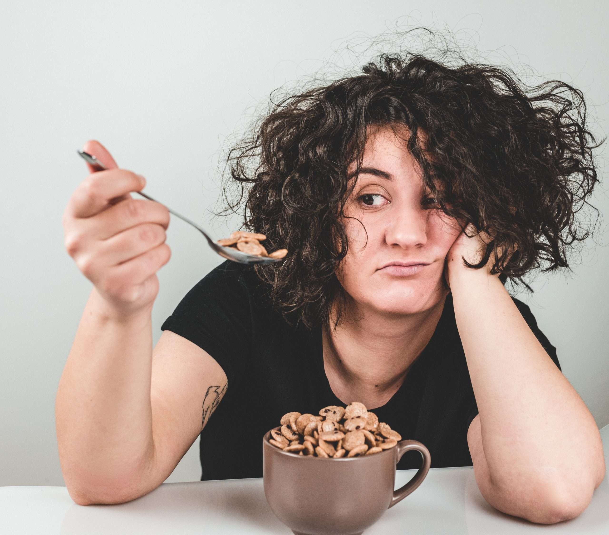 Woman looking at spoonful of cereal with quirky expression. Meant to show one way a person handles stress.