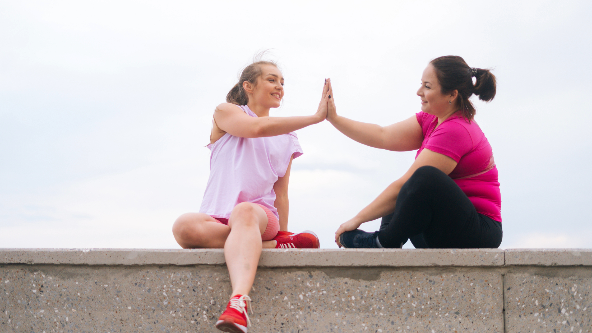 two women sitting on a ledge giving each other a high five after a personbal training session